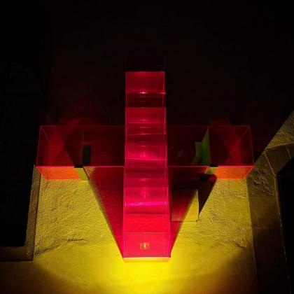 Ein Lichtkreuz von Ludger Hinse an der Kirchenwand, von unten mit einem gelben Strahler angestrahlt.